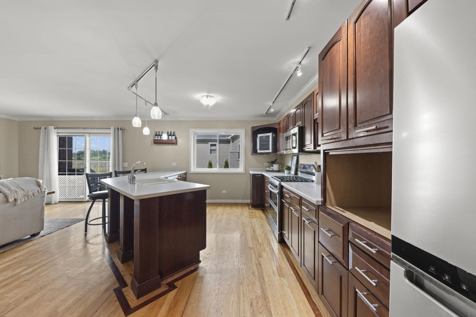 Kitchen with dark wood cabinets, central island and sink, stainless steel appliances, and hardwood floors.