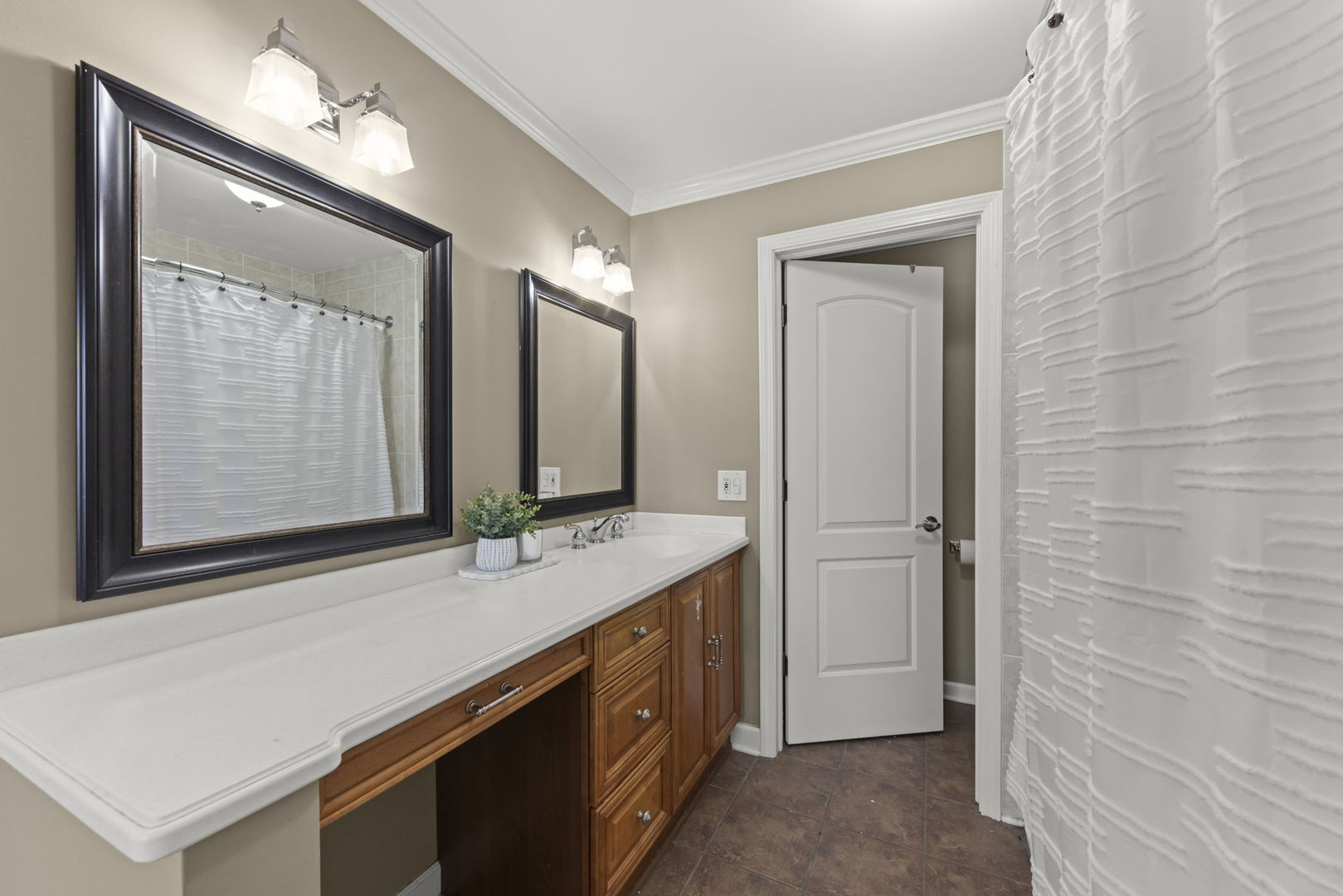 Bathroom with long white countertop, wood vanity, dark-framed mirrors, and textured white shower curtain.