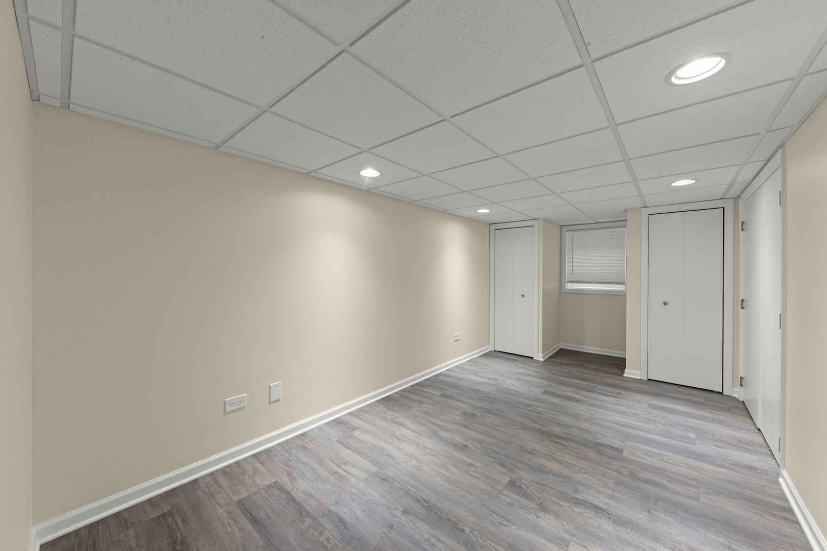 Unfurnished room with gray plank flooring, a suspended ceiling, a small window, and multiple doors.