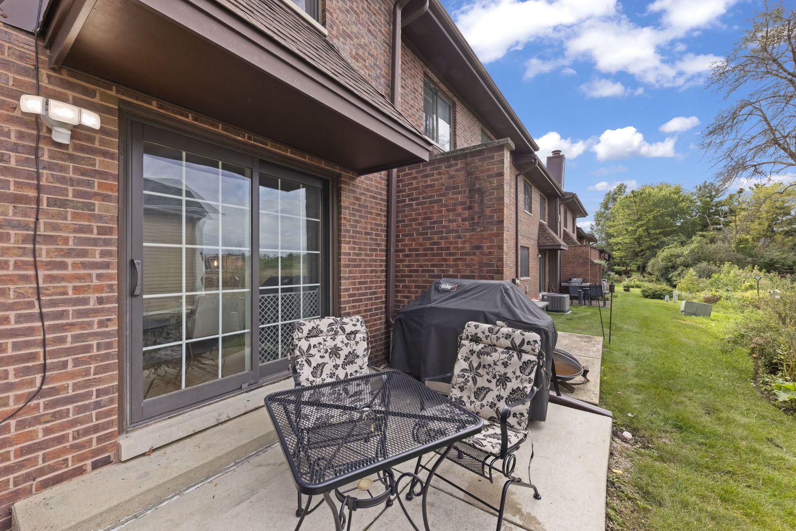 Brick townhouse patio with outdoor dining set, covered grill, and lawn alongside.