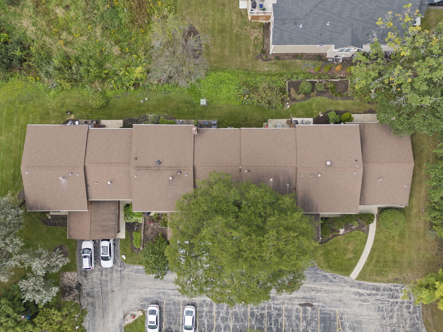 Aerial view of a home with a long shingled roof, landscaped yard, and driveway.