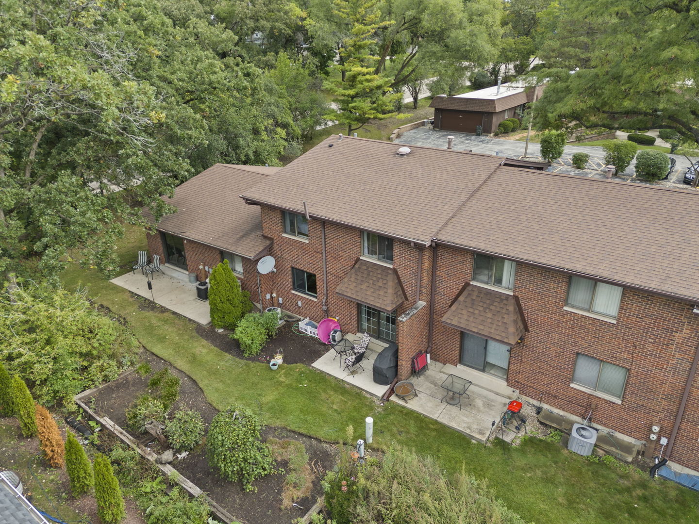 Aerial view of a brick residence with patio seating, landscaped garden, and mature trees.