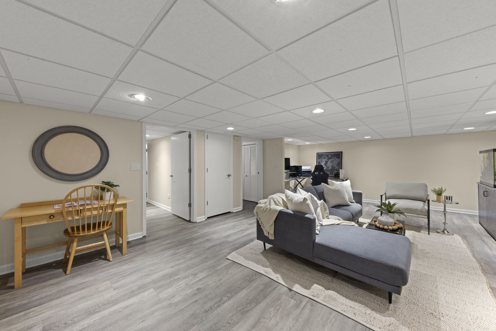 Lower-level living area with a gray sectional, armchair, pale rug, and desk.
