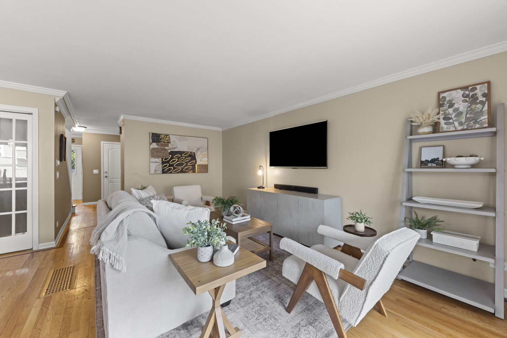Staged living room with light seating, hardwood floors, and a wall-mounted television.