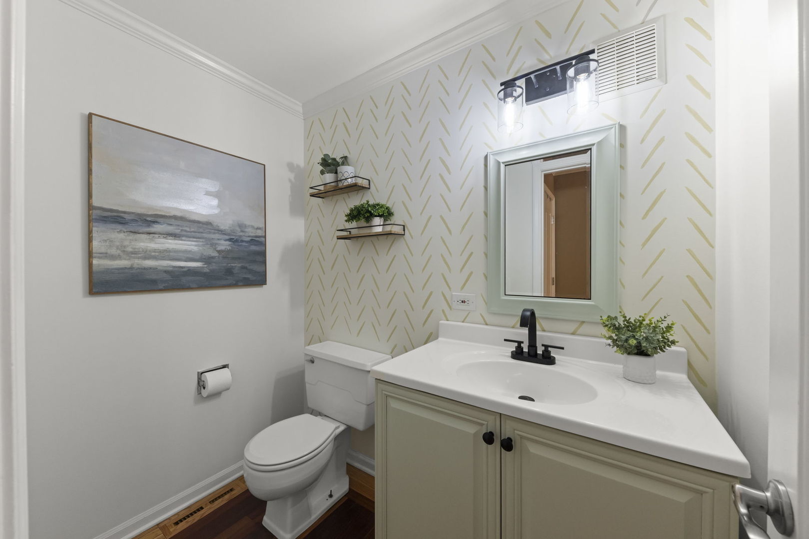 Bathroom with a pale green vanity, black faucet, framed mirror, and gold-patterned wallpaper.