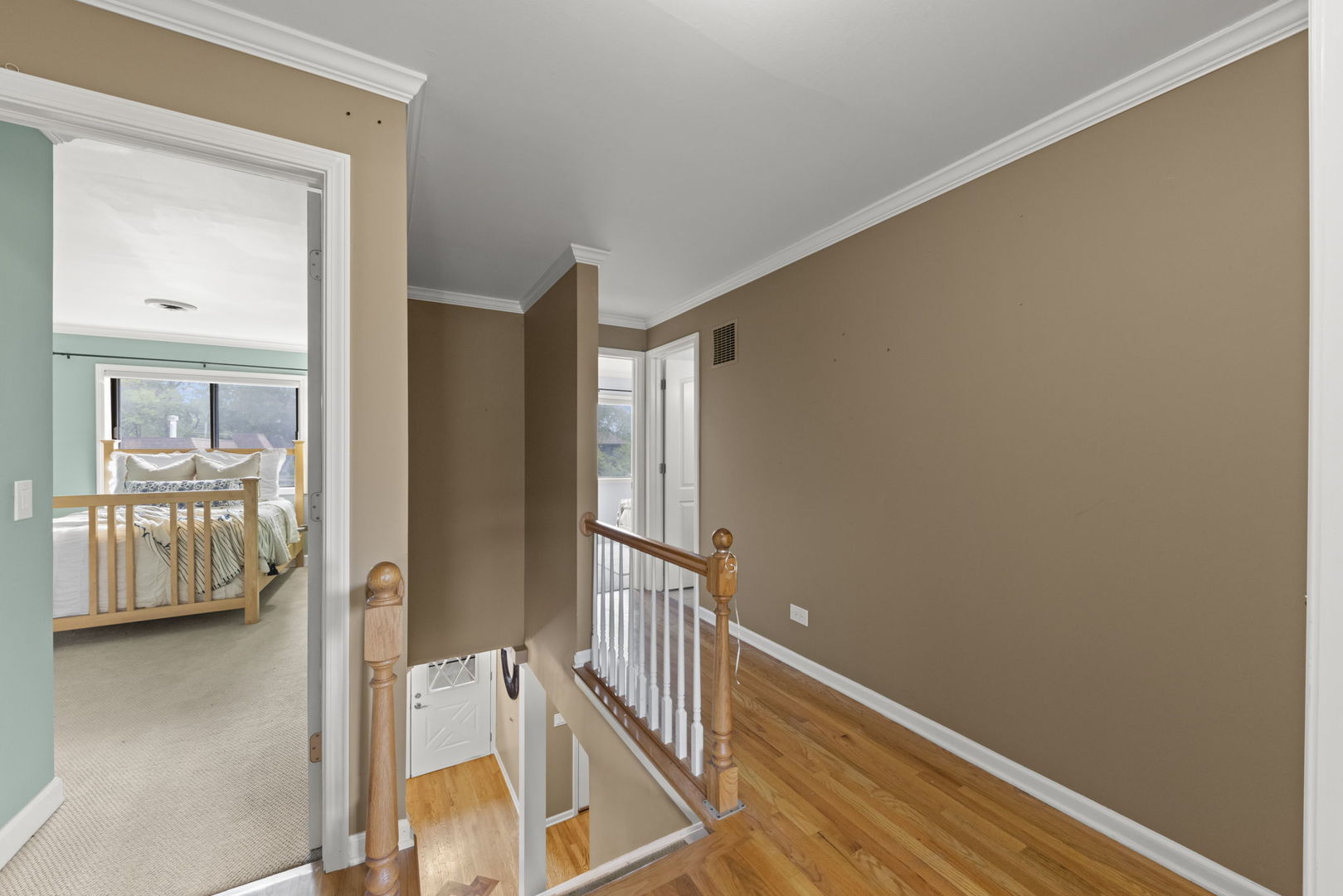 Upstairs hallway with hardwood floors, white stair balusters, and a view into a bedroom.