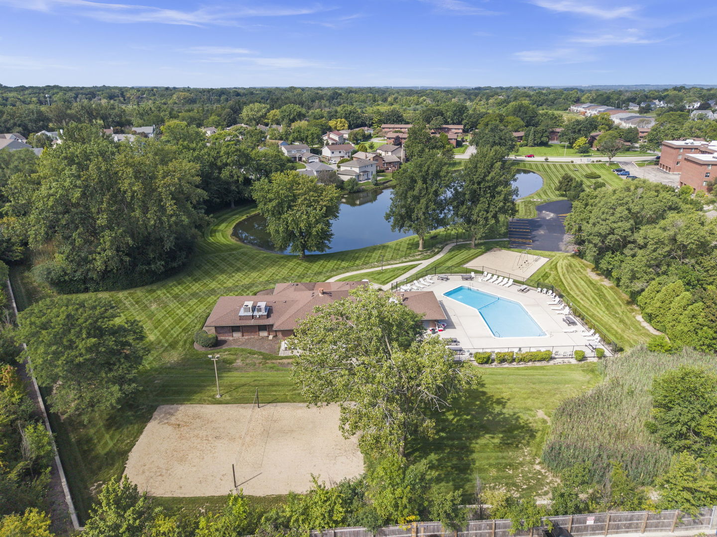 Aerial view of a community pool and clubhouse beside a pond and landscaped grounds