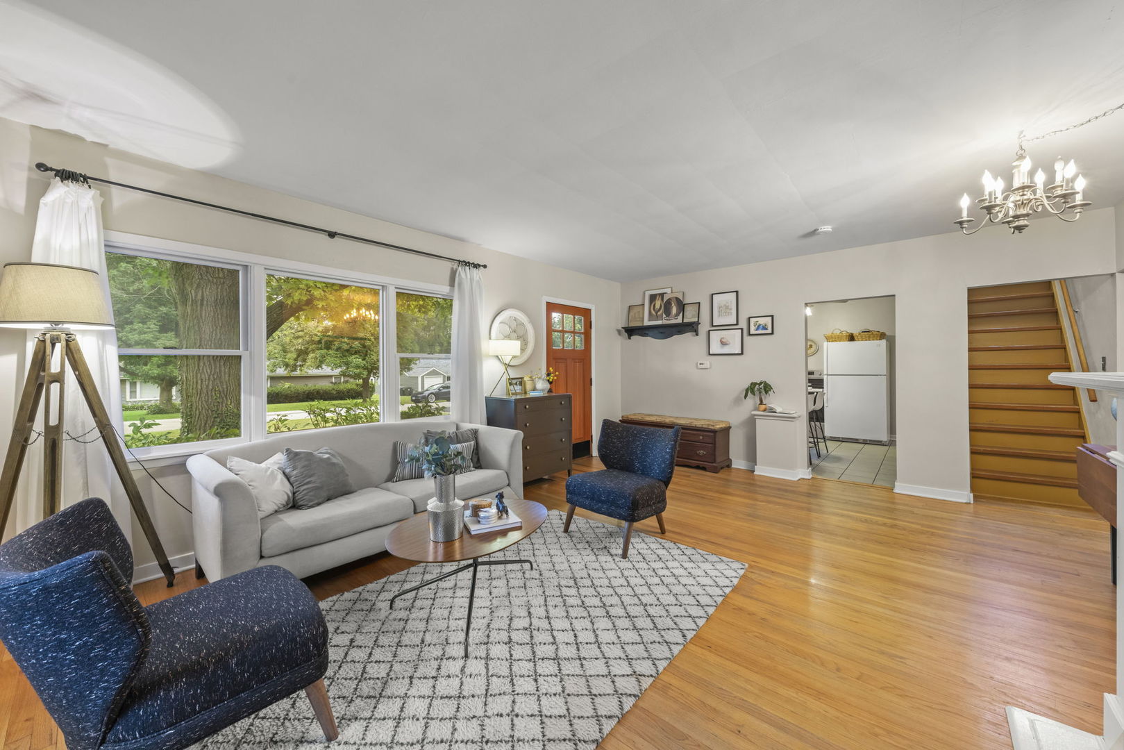 Living room with hardwood floors, large windows, gray sofa, blue chairs, and a patterned rug.