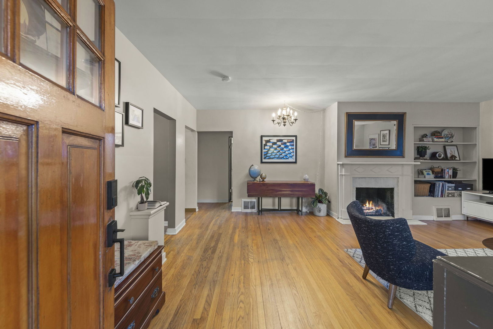 Living room with hardwood floors, a wood entry door, and a white fireplace.