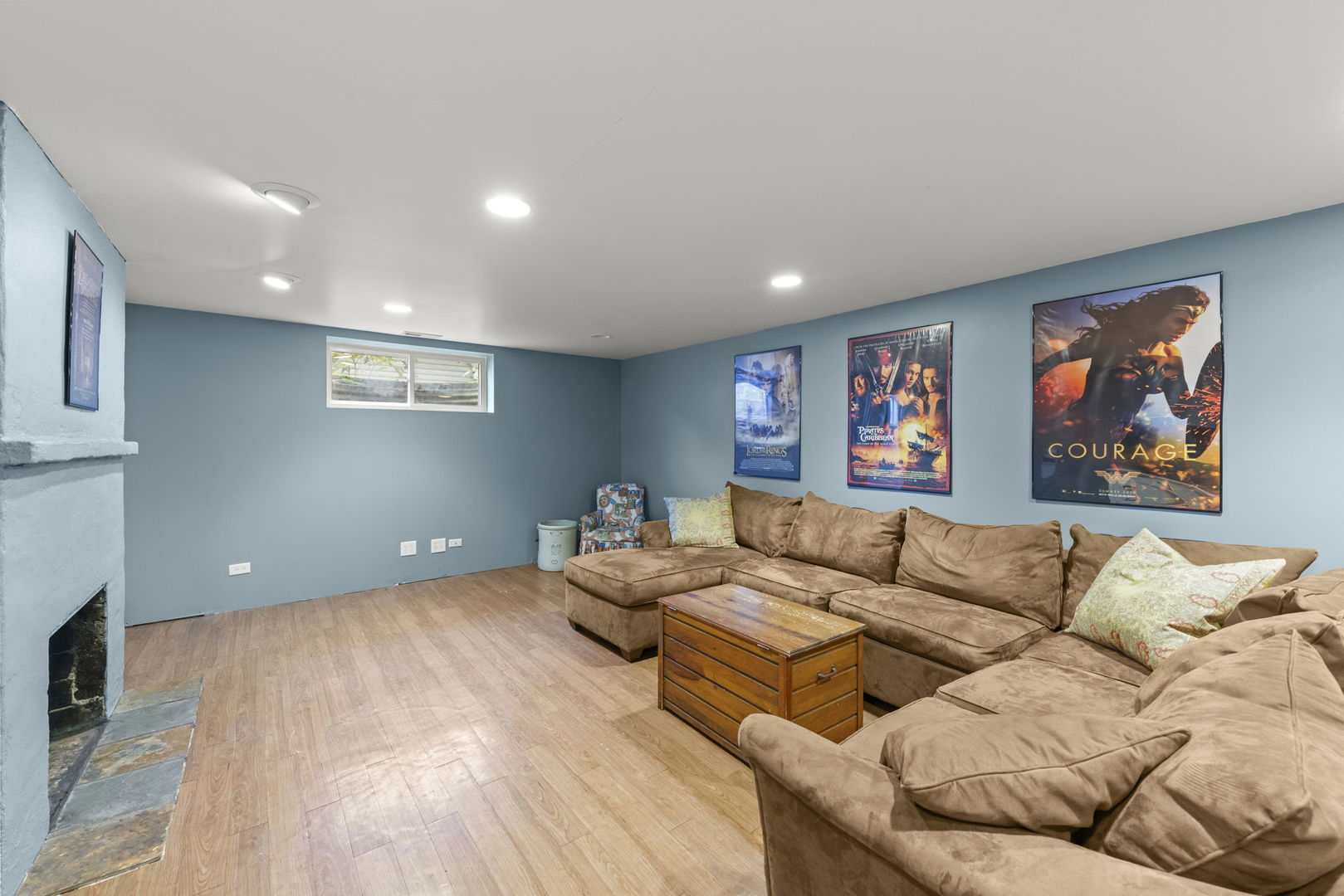 Basement recreation room with a tan sectional, fireplace, and movie posters on blue walls.