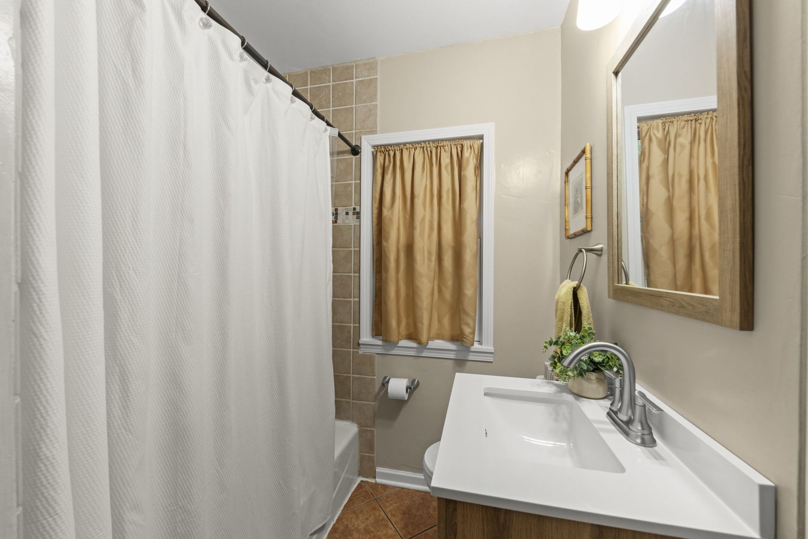 Bathroom with a white vanity, tiled shower, and gold-curtained window.