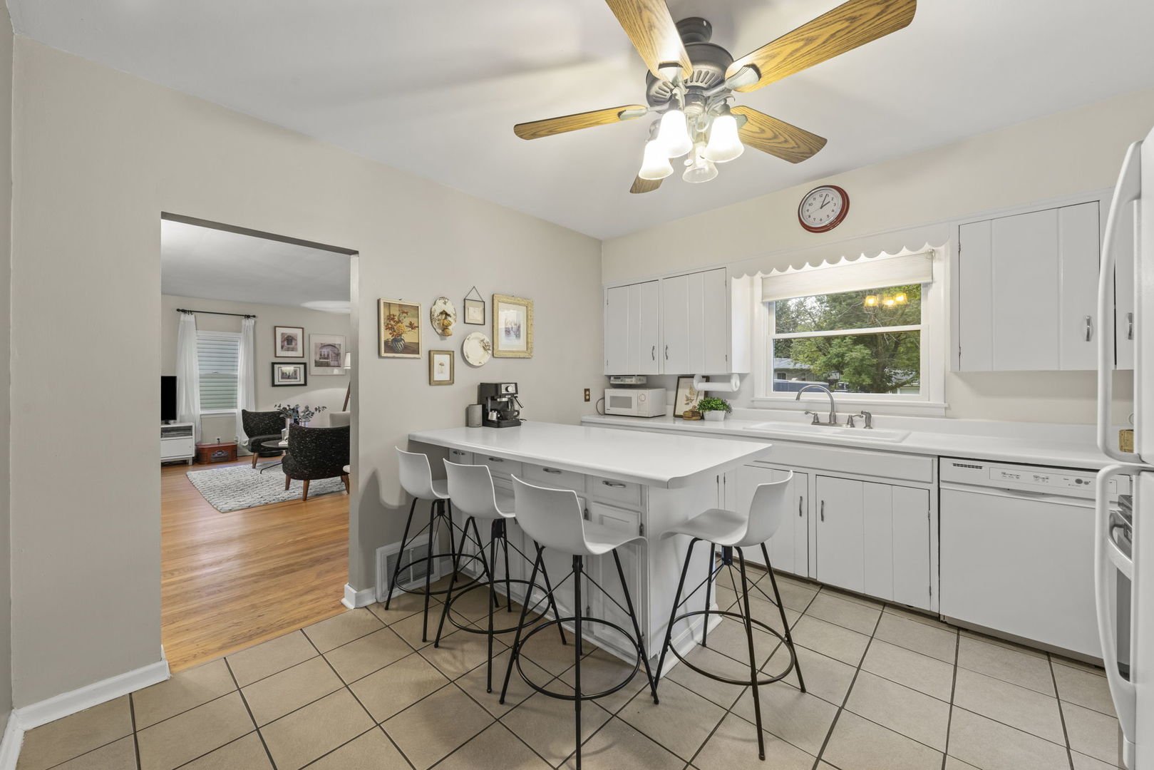 Kitchen with white cabinetry, tiled floors, and a peninsula with four bar stools overlooking the living room.