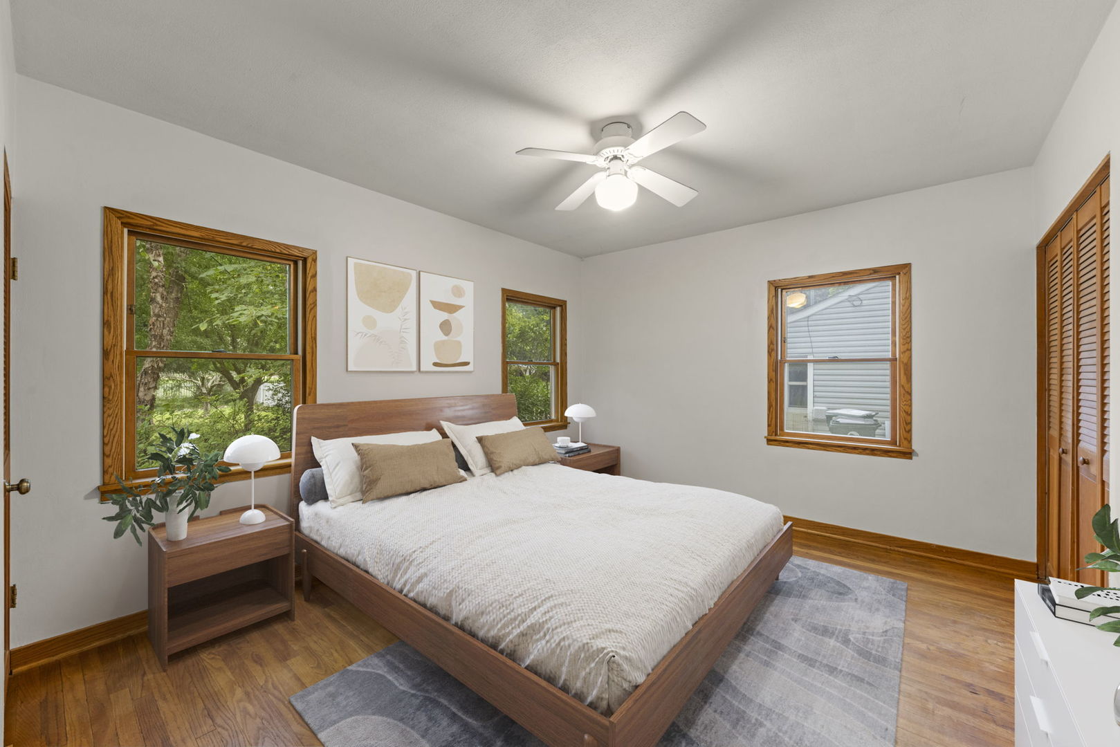 Bedroom with a large wooden bed, gray rug, and three wood-trimmed windows.