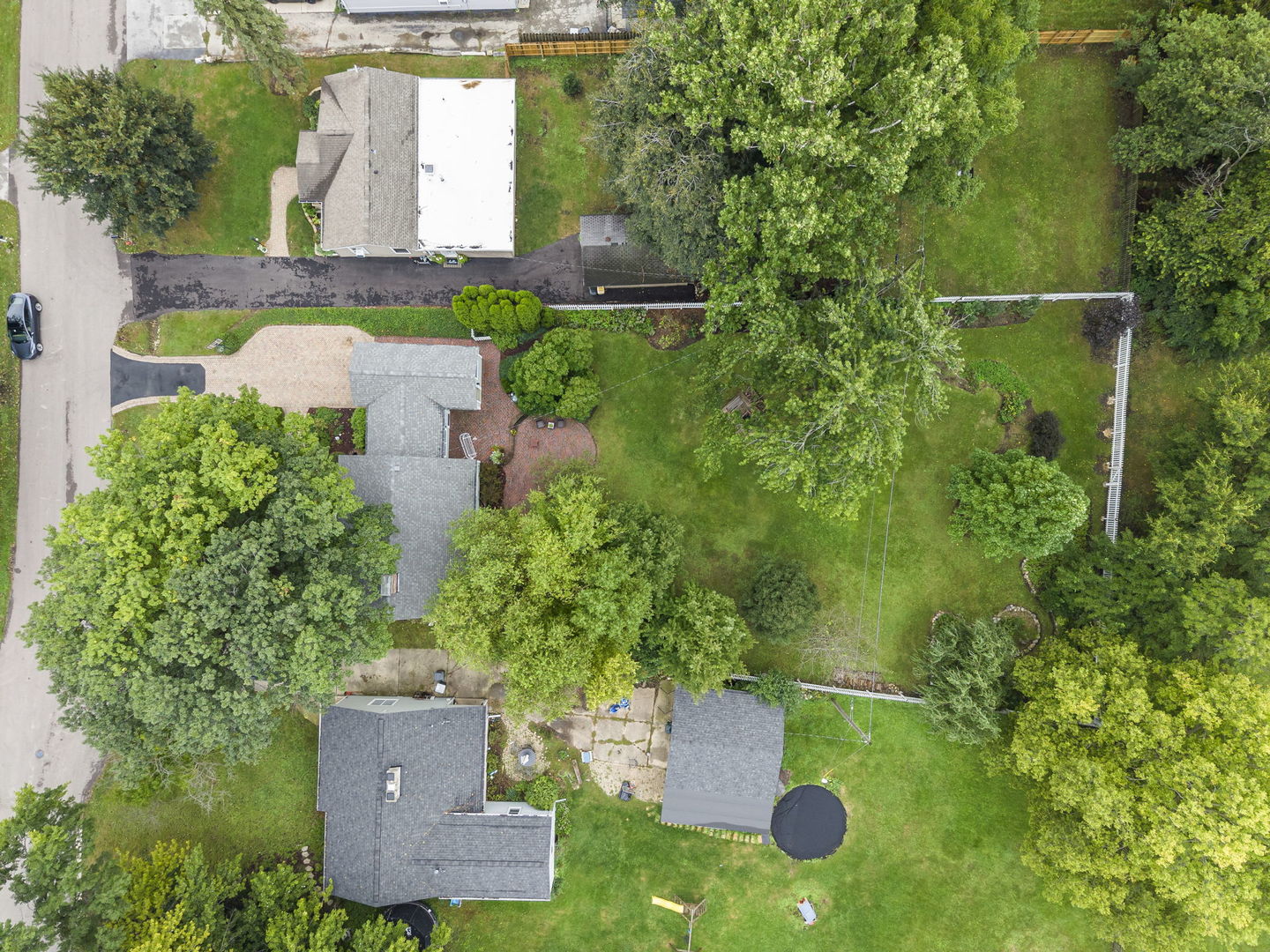 Aerial view of a tree-filled residential lot with a large lawn and round trampoline.