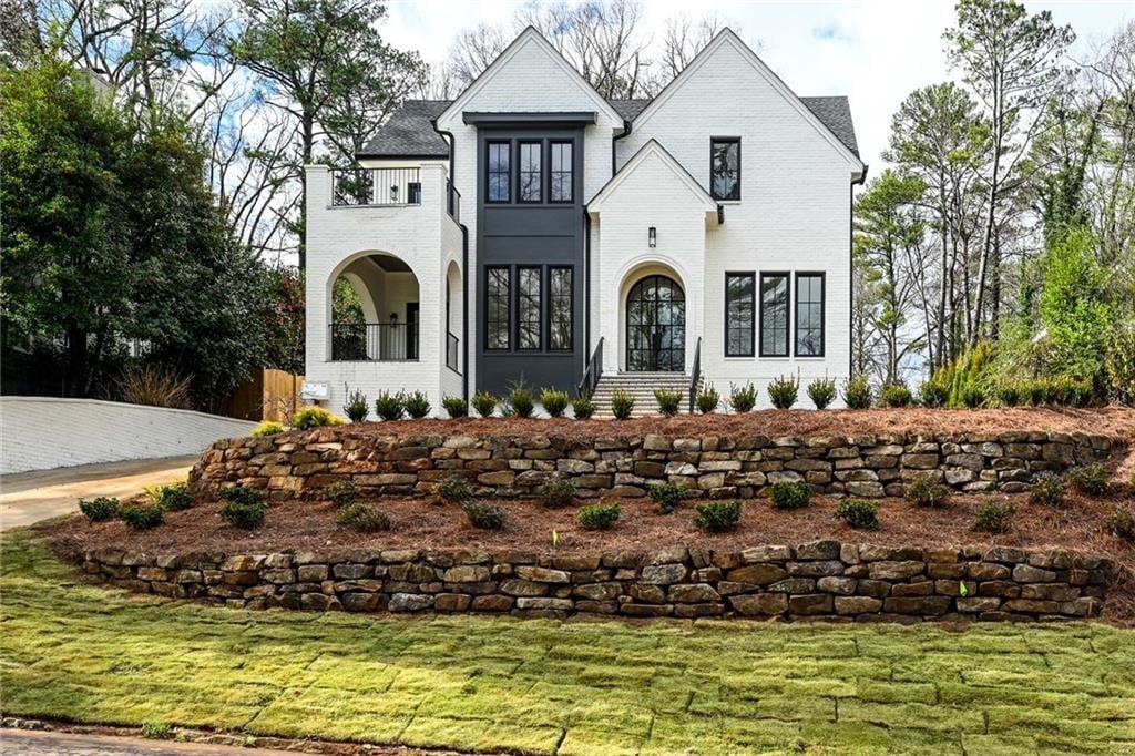White brick house with dark windows and arched entryways above tiered stone retaining walls.