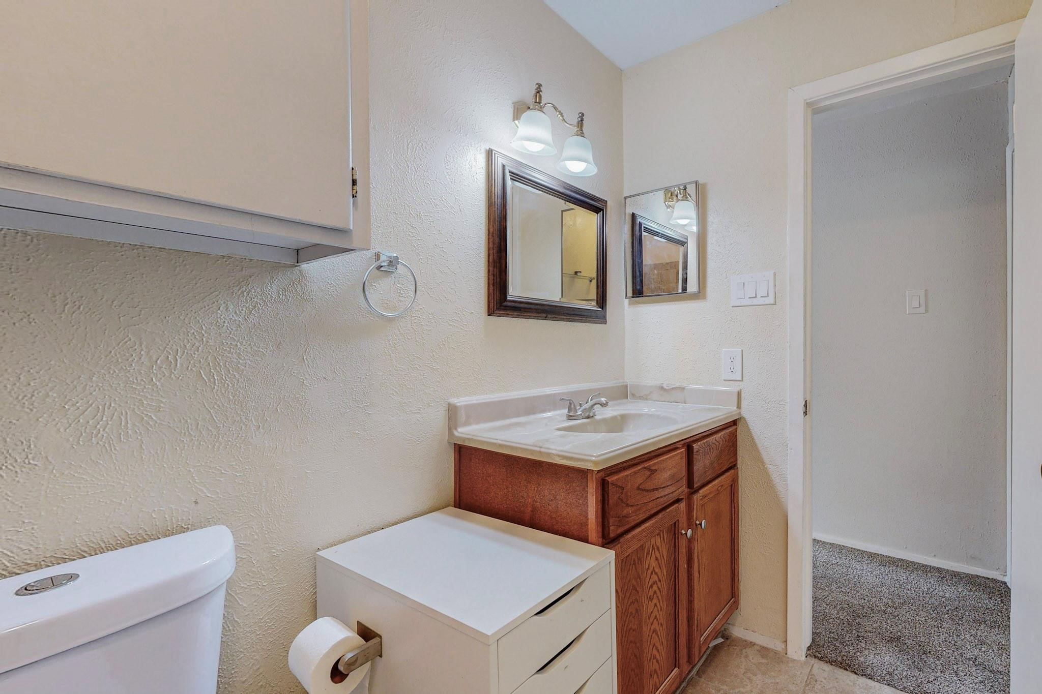 Bathroom with a wood vanity, white sink, framed mirrors, and part of a toilet.