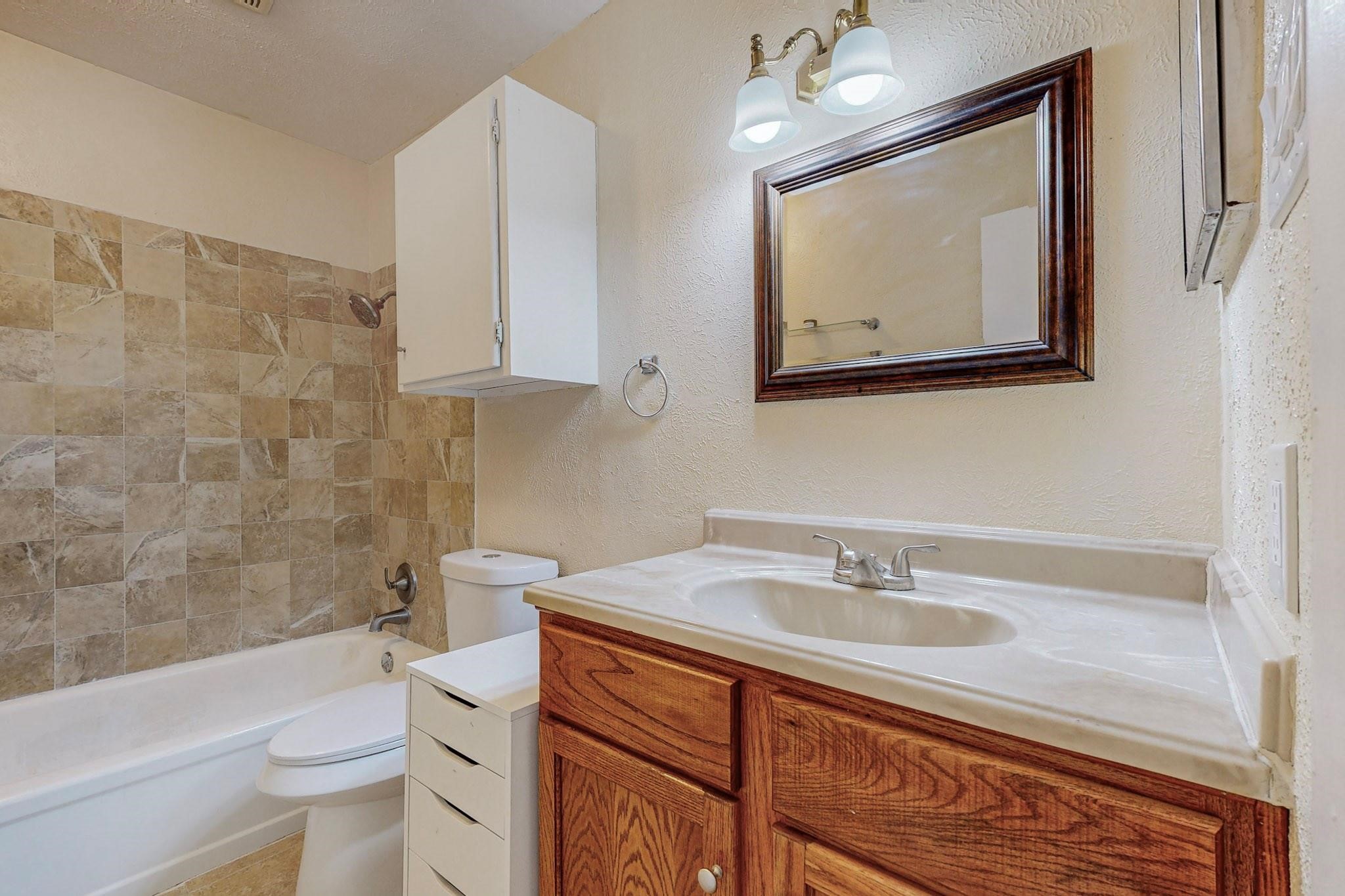 Bathroom with a tiled tub and shower beside a wood vanity and framed mirror.