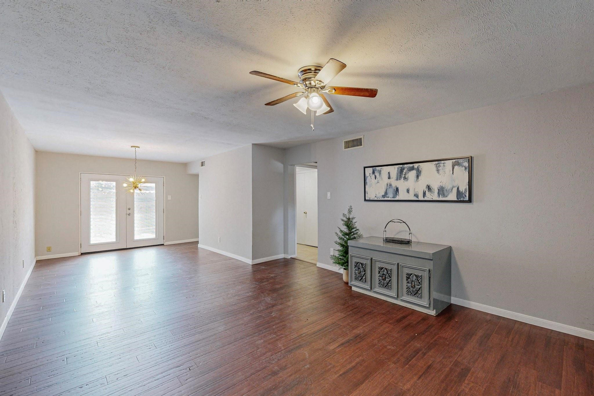 Living room with dark wood floors, French doors, and a ceiling fan with lights.