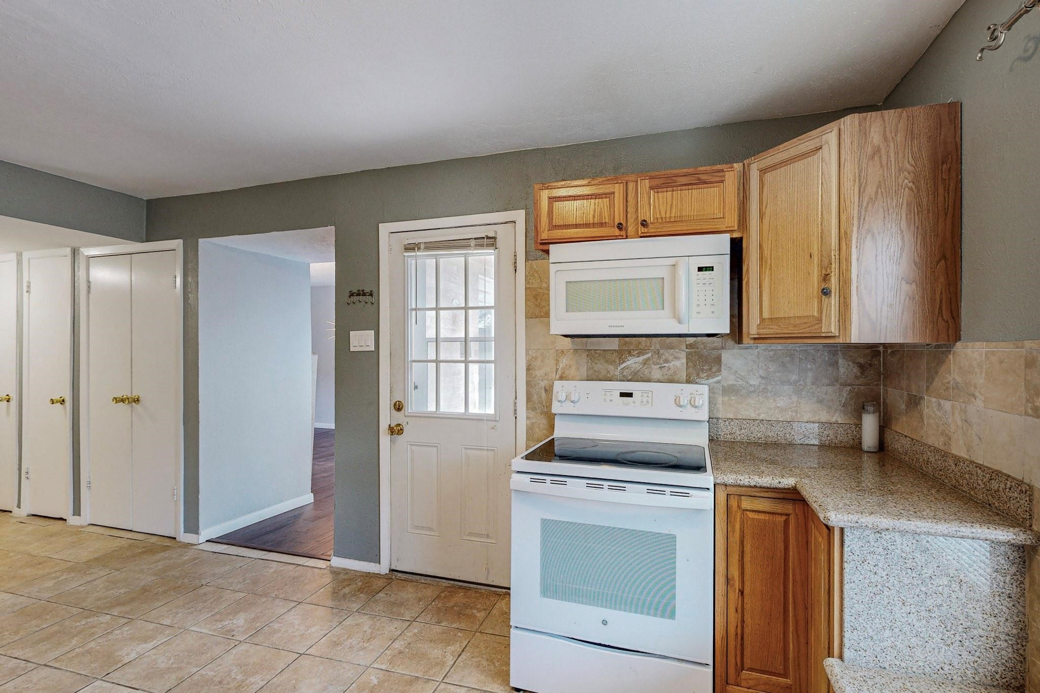 Kitchen with wood cabinets, white range and microwave, and a glass-paneled door.