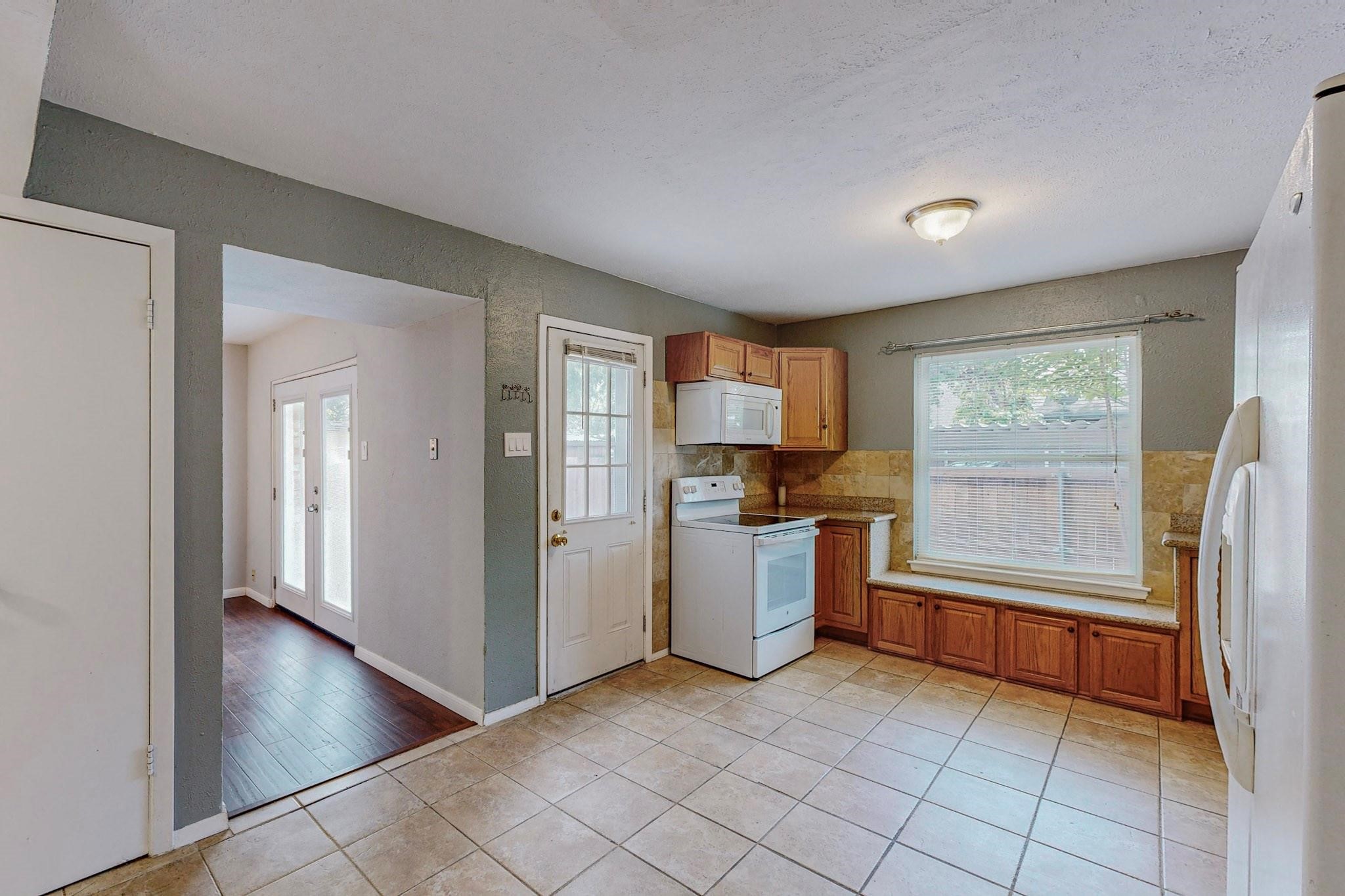 Kitchen with wood cabinets, white appliances, and a large window above the counter.