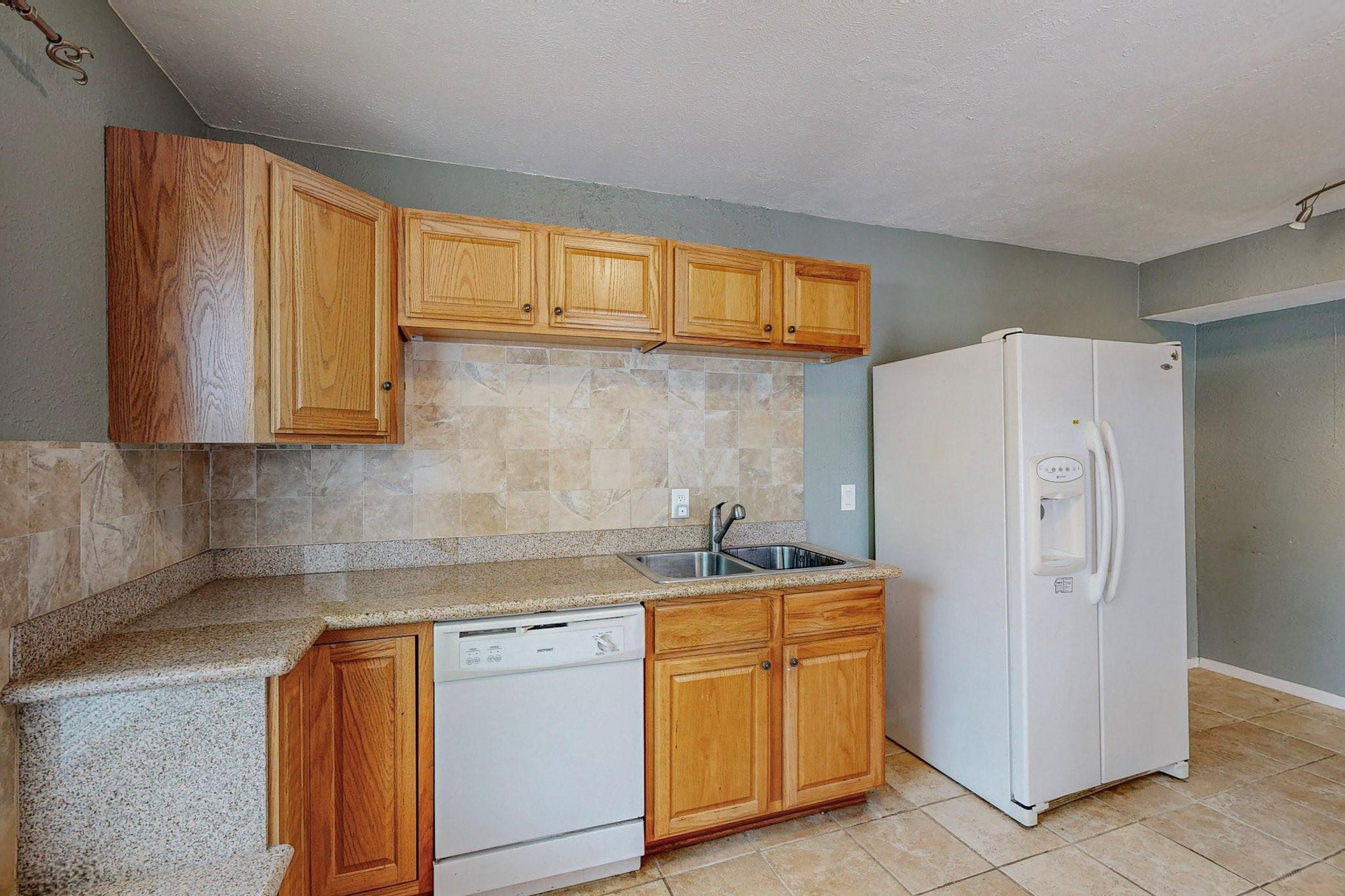 Kitchen with wood cabinets, tile backsplash, double sink, dishwasher, and white refrigerator.