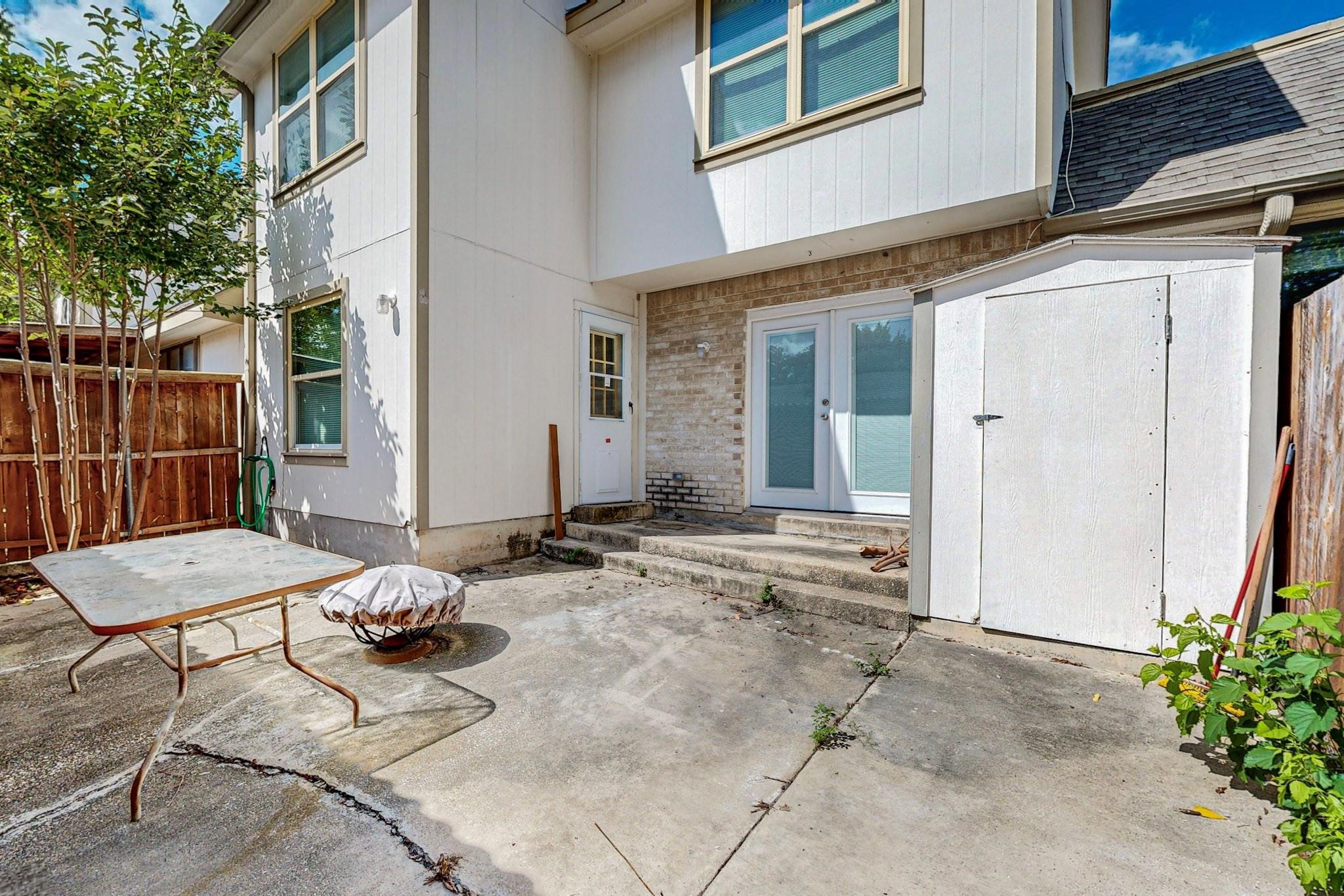 Concrete backyard patio with sliding glass doors, a large white storage shed, and a folding table.