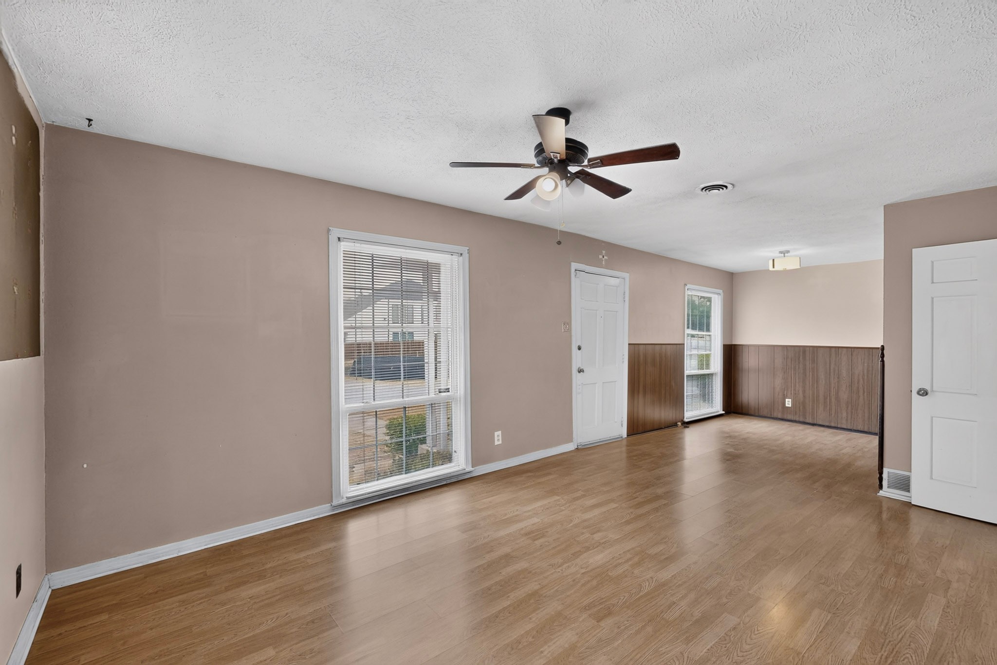 Empty living room with wood flooring, wainscoting, two windows, and a ceiling fan.