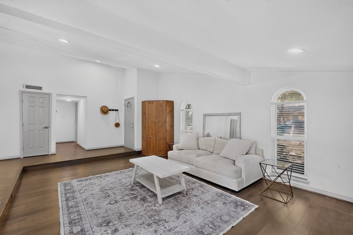 Furnished living room with a white sofa, patterned rug, wood floors, and arched windows.