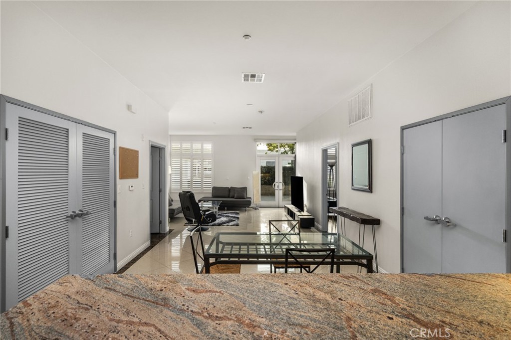 Open-plan living and dining area with a glass table, gray louvered doors, and granite counter.