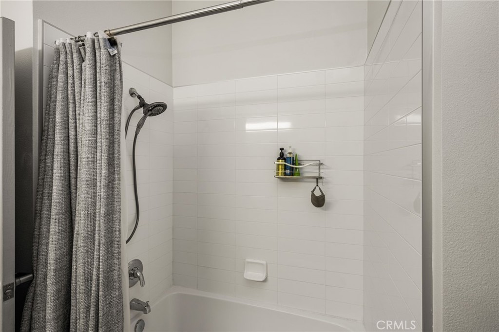 White tiled bathtub and shower with a gray curtain and toiletries on a wall shelf.