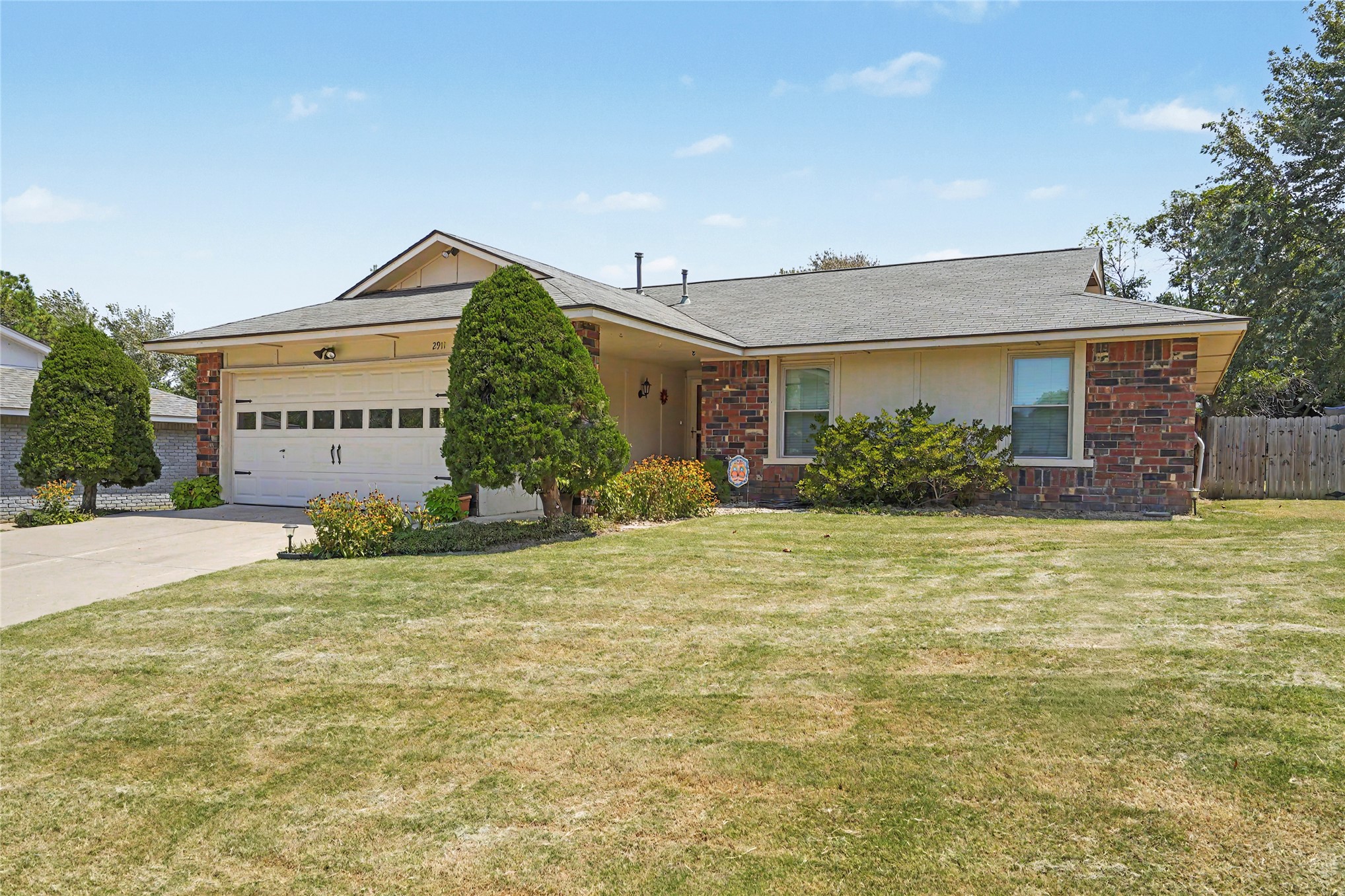 Single-story brick home with an attached white garage, front lawn, and trimmed shrubs.