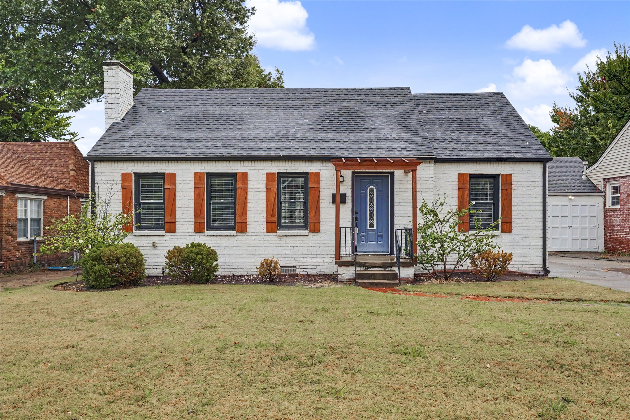 White brick house with wooden shutters, a blue front door, and a broad front lawn.