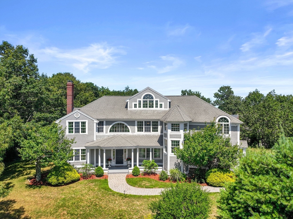 Large gray-shingled home with white trim, covered porch, landscaped front garden, and curved stone walkway.