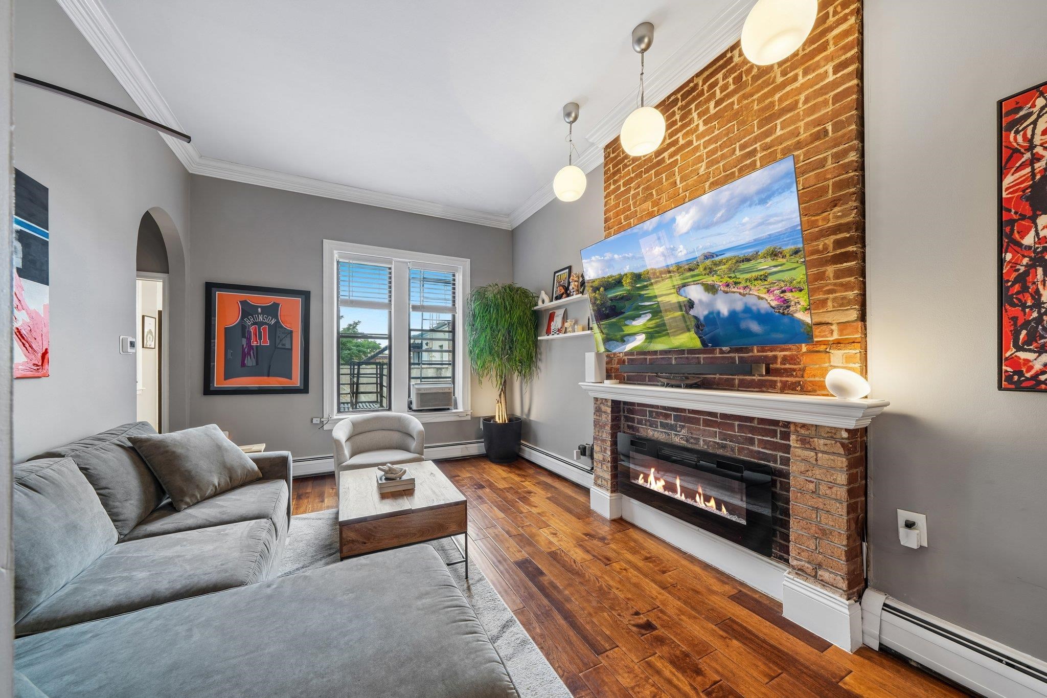 Furnished living room with a gray sectional, wood floors, and a brick fireplace.