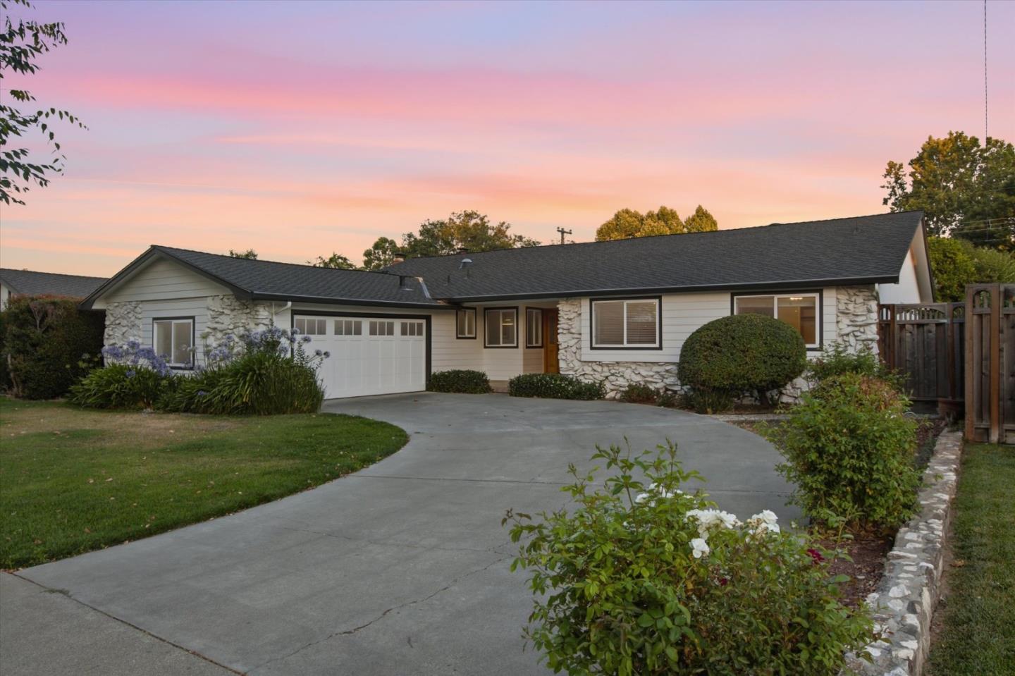 Single-story house with stone accents, attached garage, and landscaped driveway beneath a pink dusk sky.