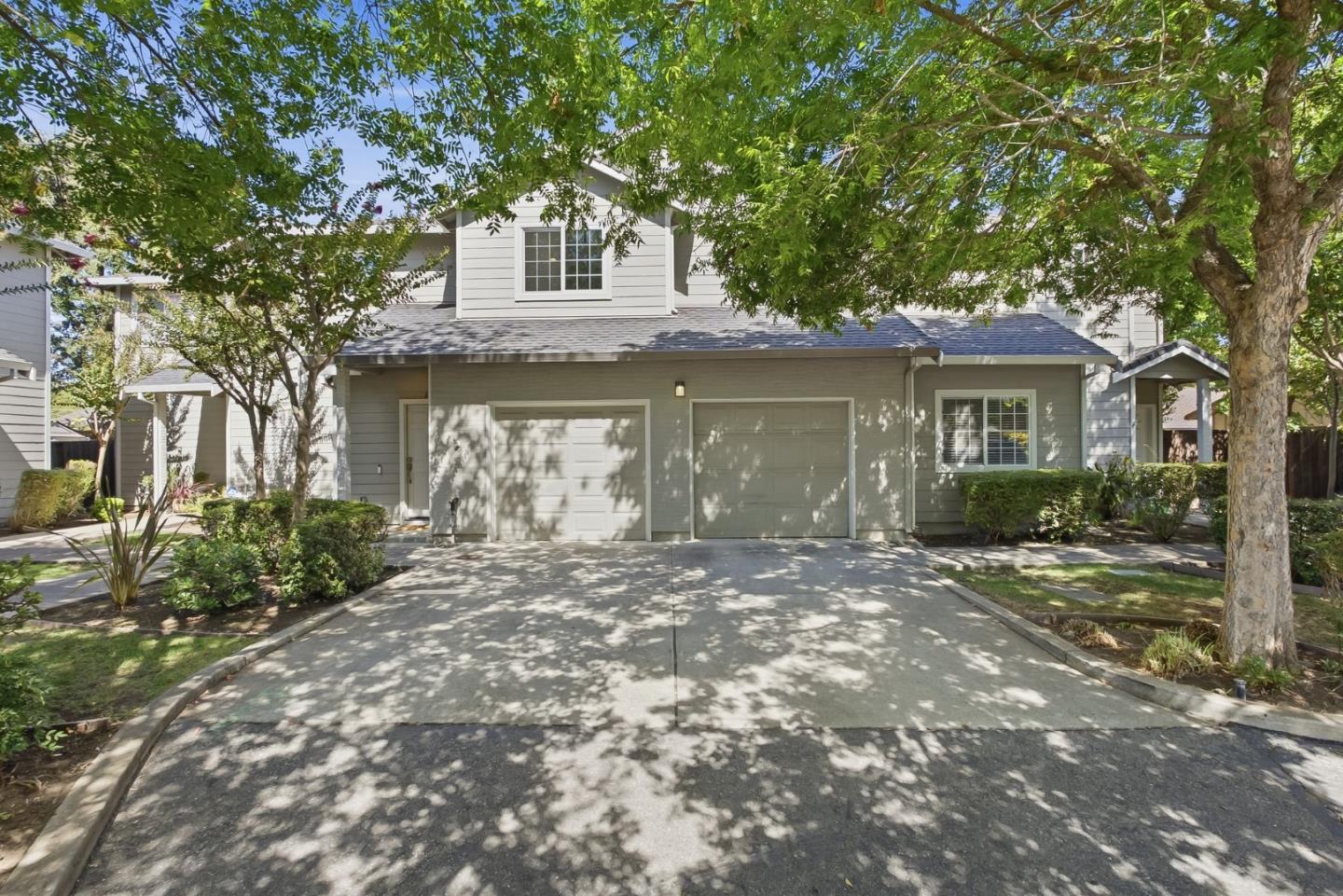 Two-story gray-and-white house with an attached garage and a tree-shaded driveway.