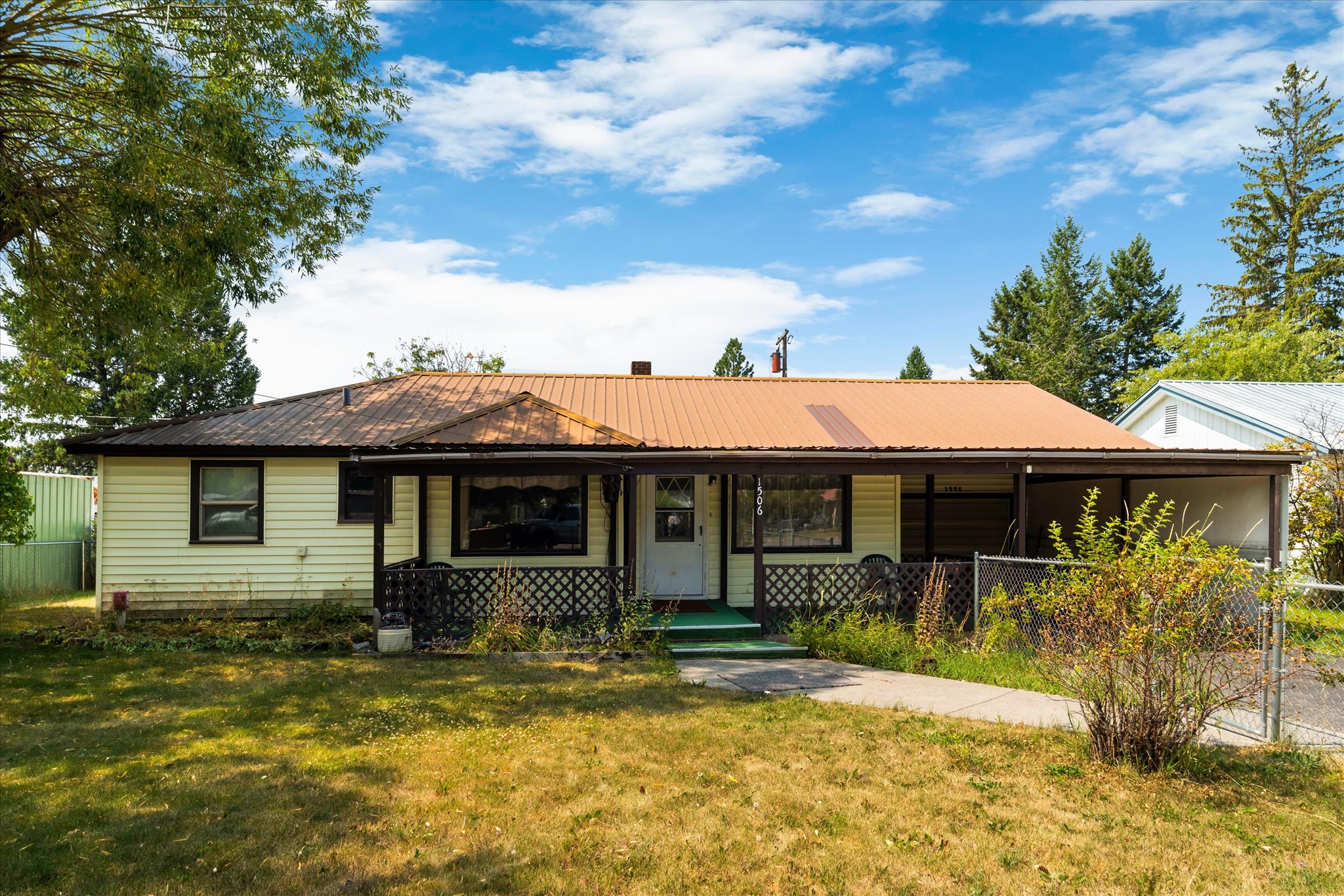 Single-story yellow house with a copper-colored metal roof, covered porch, and fenced front yard.