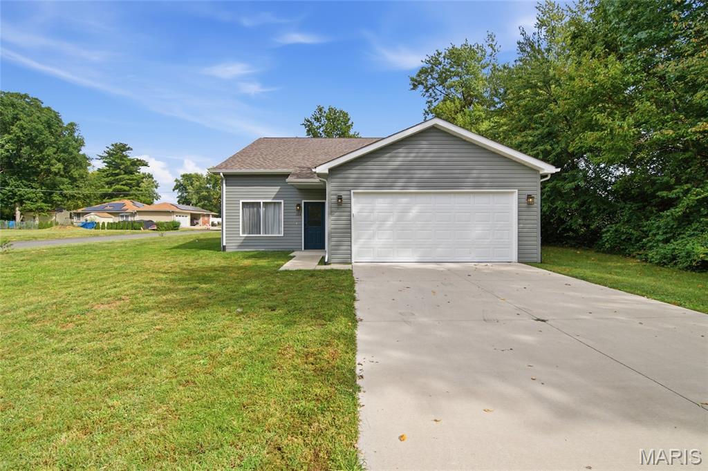 Gray single-story house with a white double garage door, wide driveway, and green lawn.