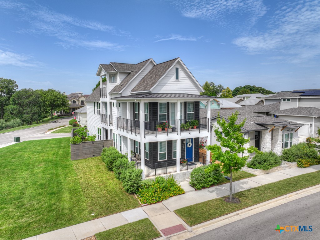 Two-story white house with wraparound balconies, a blue front door, and landscaped lawn.