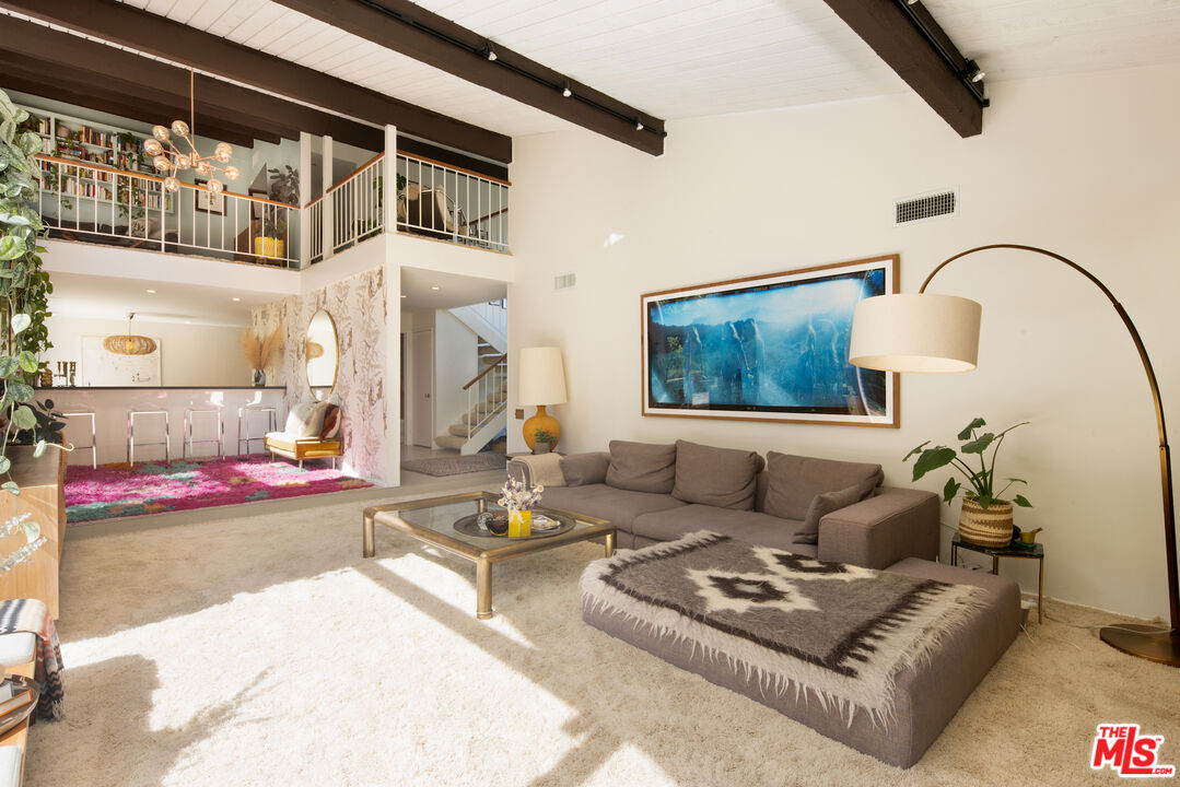 Living room with a double-height beamed ceiling, upper-level loft, and adjoining bar area.