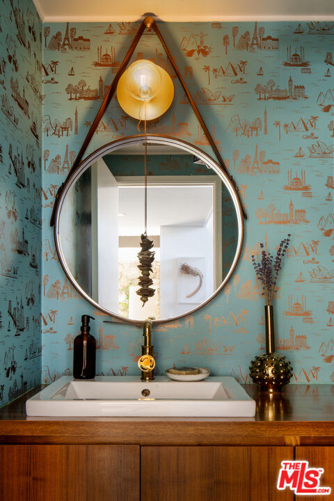 Powder room vanity with patterned turquoise wallpaper, a round mirror, and a globe pendant light.
