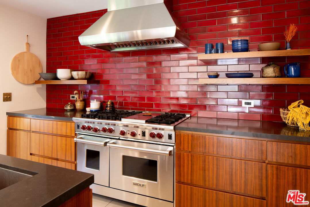 Kitchen with a stainless steel range, glossy red tile backsplash, and walnut cabinetry.