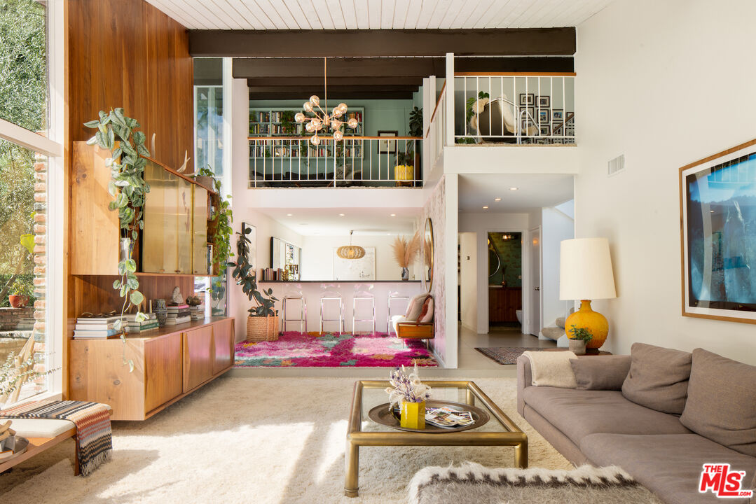 Double-height living room with a wood-paneled built-in, gray sofa, and colorful rug.