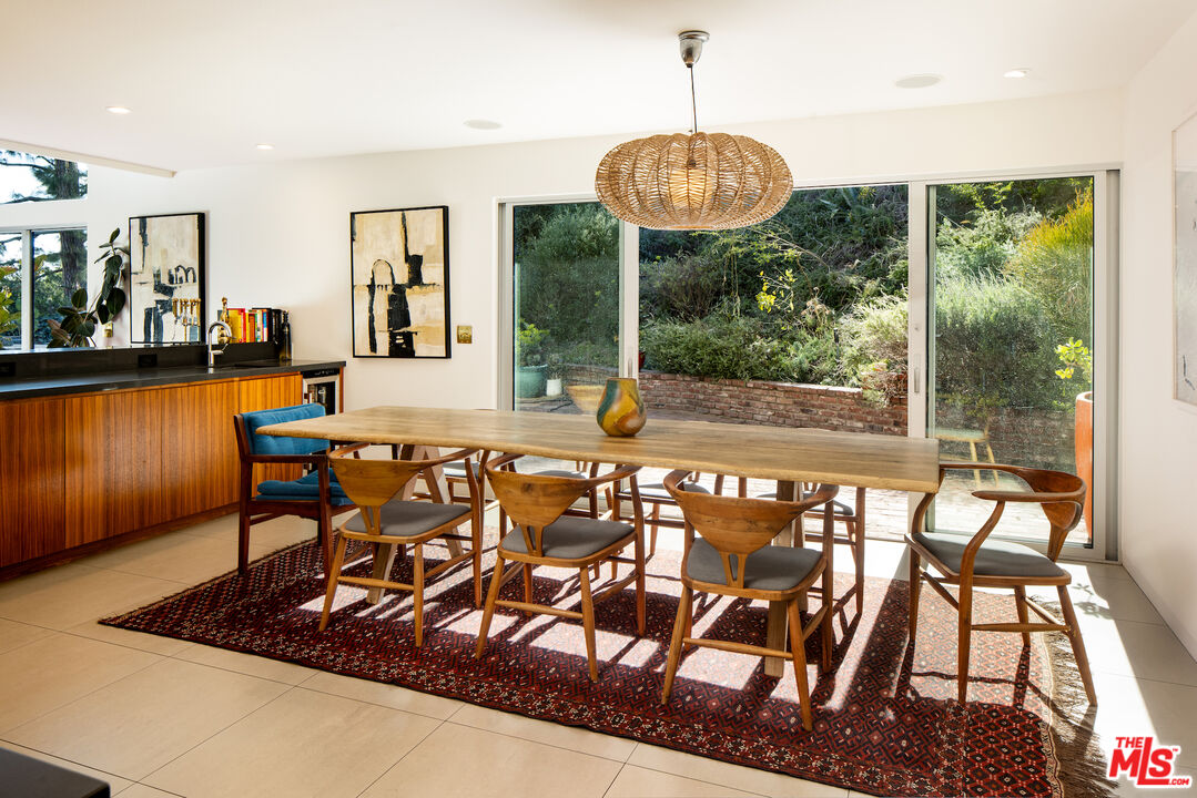 Dining room with a long wooden table, woven pendant, and sliding glass doors overlooking a garden.