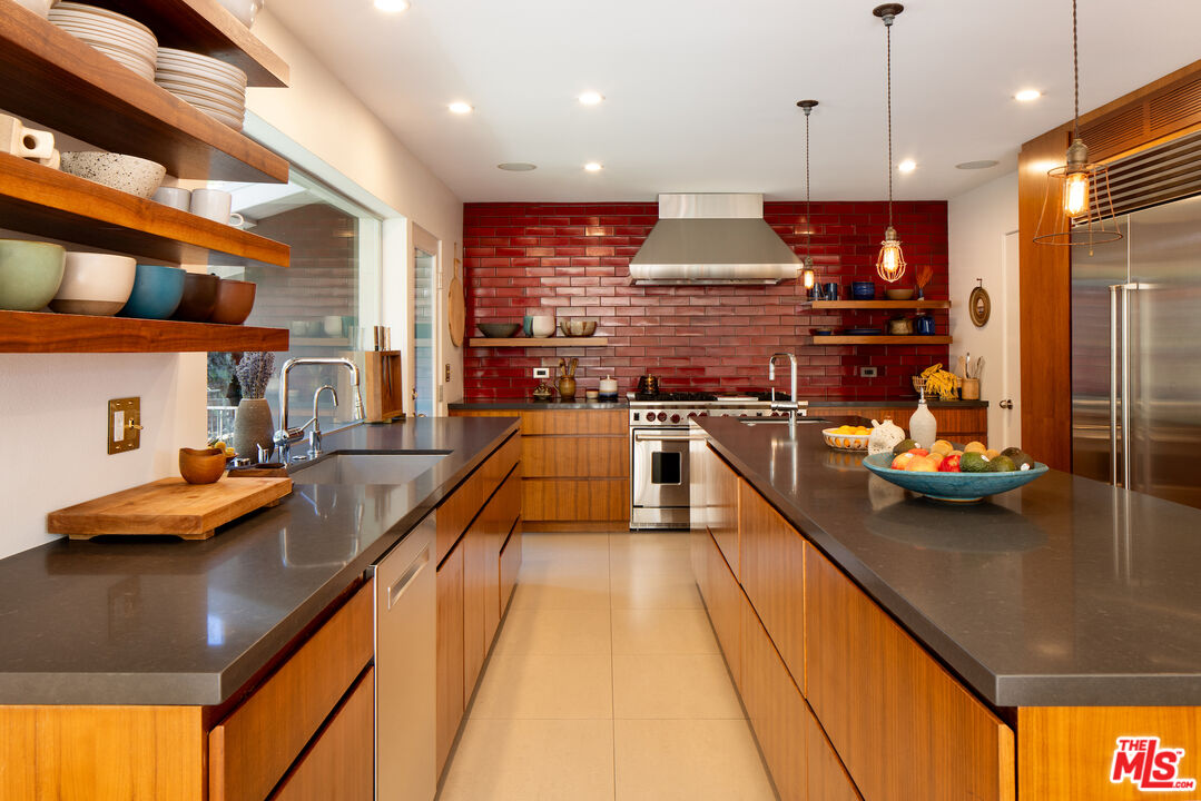 Modern kitchen with warm wood cabinets, dark stone counters, and a red tile backsplash.