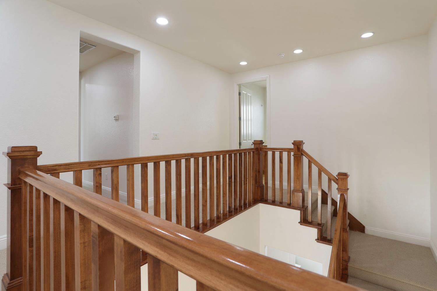 Upstairs landing with a polished wood railing surrounding the stairwell and beige carpet.
