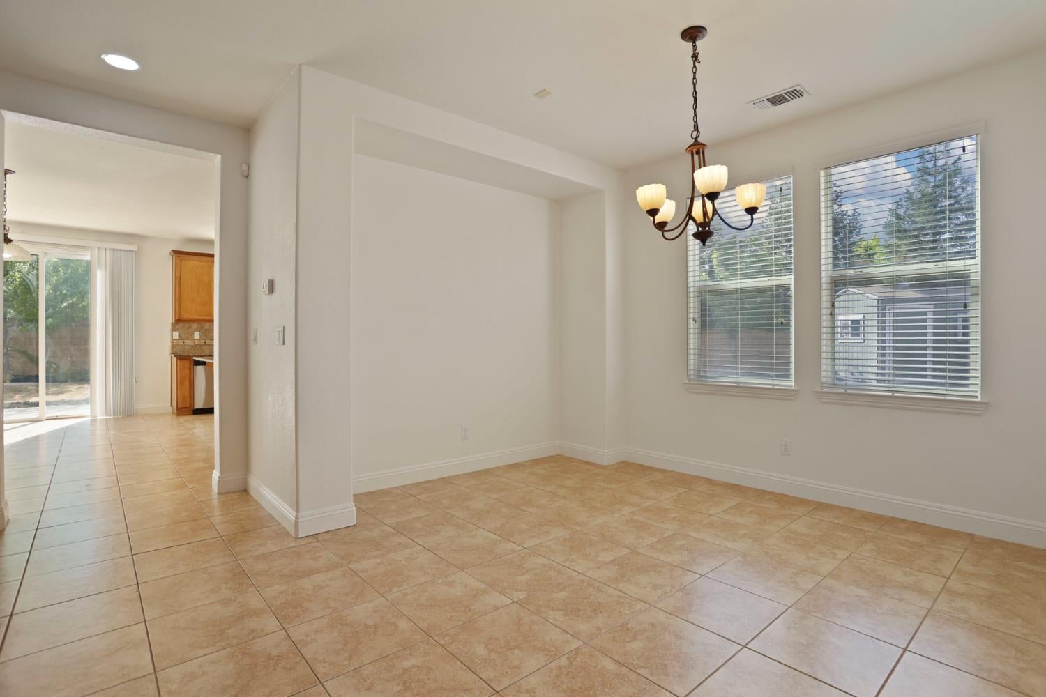 Empty dining area with tan tile floors, a chandelier, and two windows with blinds.