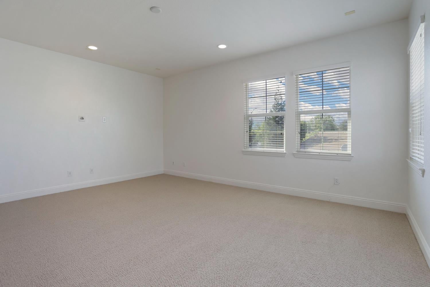 Empty carpeted room with white walls and multiple windows with blinds.