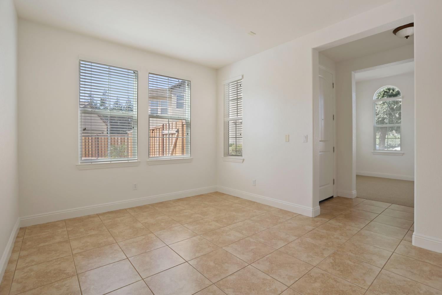 Empty tiled room with three windows and a wide opening to an adjoining carpeted room.