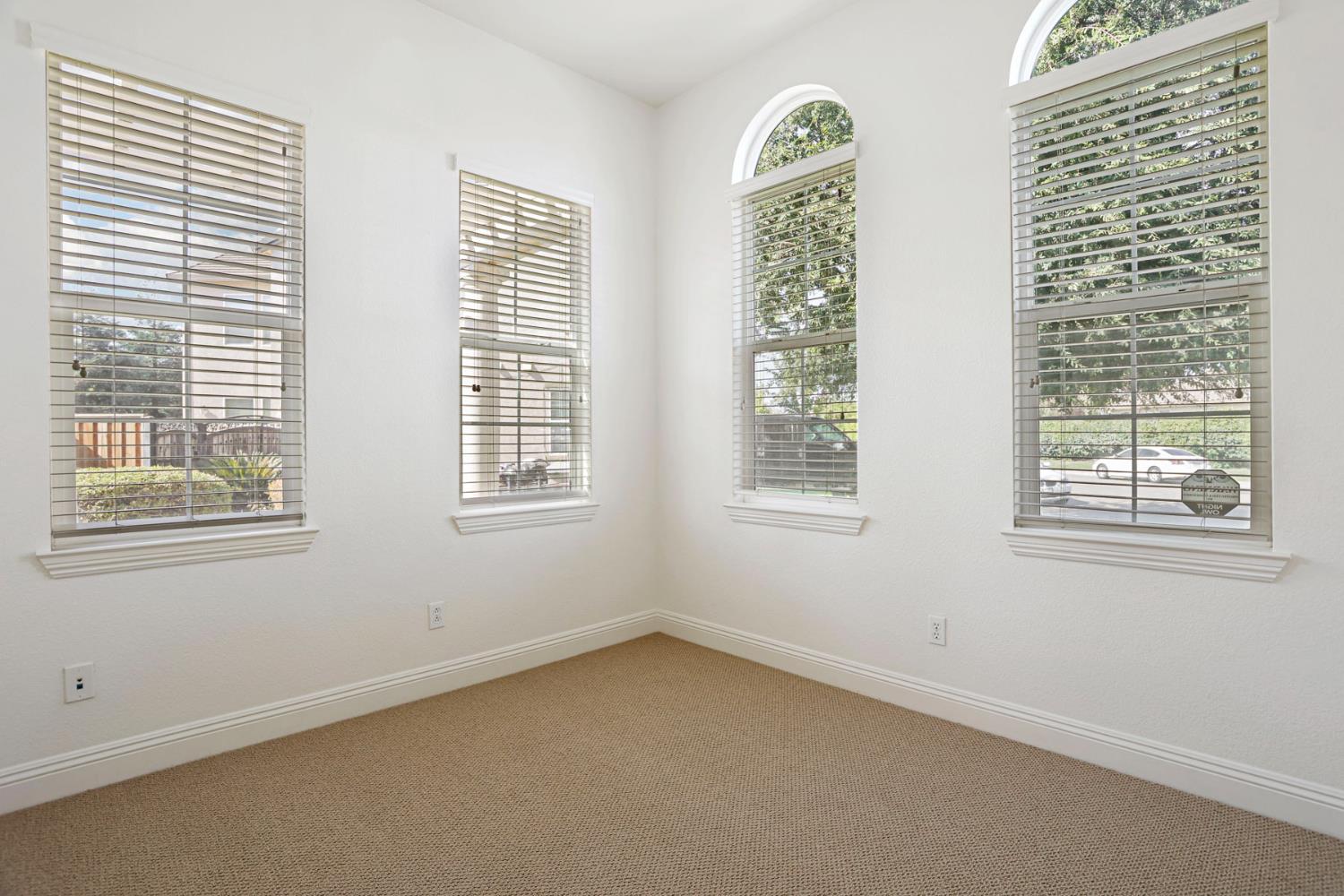 Empty carpeted room with four blind-covered windows, including two with arched tops.